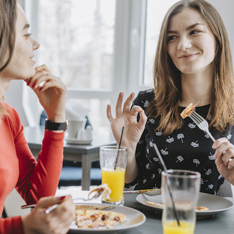 two women eating at a restaurant, one giving the "ok" sign for delicious food.