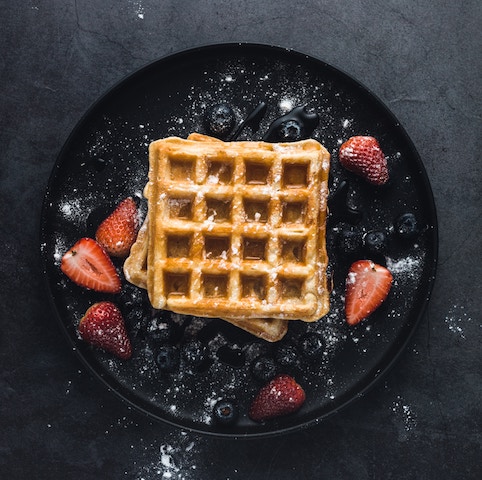 A Belgian waffle covered in fruit, sugar and syrup.