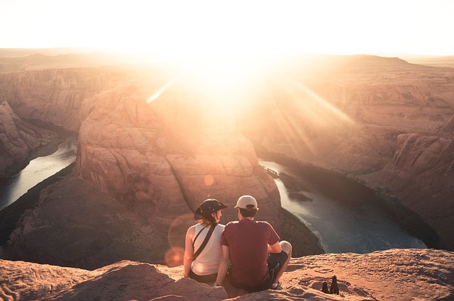Couple sitting above looking down into grand canyon during sunset.