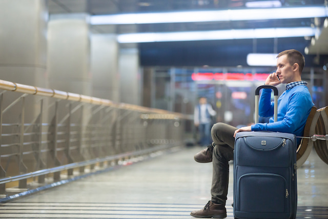 traveler waiting while using charging cable on his phone.