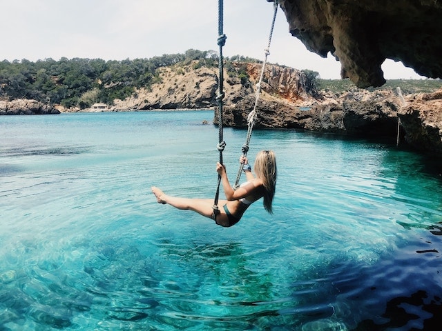 A woman swinging into blue waters in Ibiza, Spain. Great to relax post break up. 