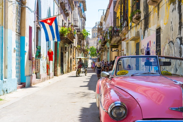 a street of Havana with vintage pink car and many colorful buildings. 